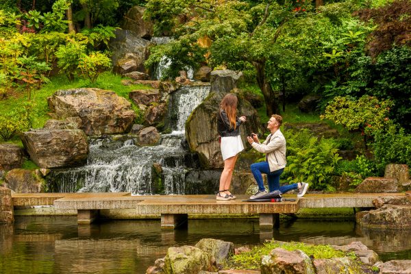 A man down on his knee holding a box with an engagement ring in front of his girlfriend during the actual proposal in Kyoto Gardens