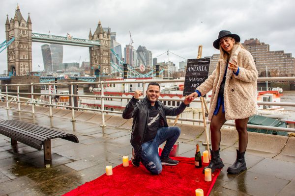 A man rasing his hand in the victory gesture after the successful surprise proposal in front of the Tower Bridge