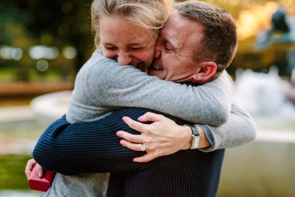 A close-up shot of a newly engaged woman smiling joyfully while tightly hugging her partner. after the surprise proposal in Hyde Park