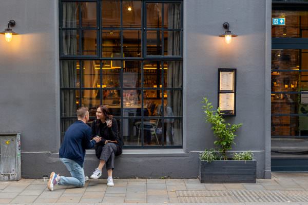 The happy couple sharing a laugh outside a charming London café directly after their surprise proposal.