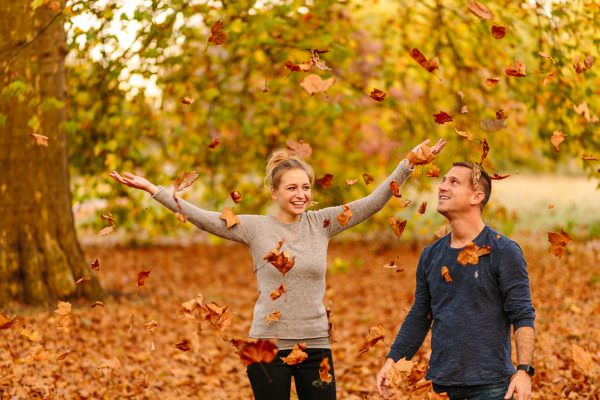 A playful couple throwing crisp autumn leaves into the air during a golden hour shoot moments before the actually proposal.