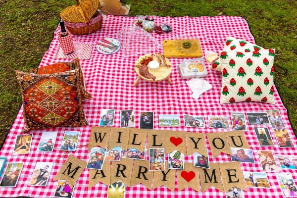 A luxury surprise engagement setup in London, featuring a striking "Marry Me" sign seamlessly integrated into a romantic outdoor picnic layout.