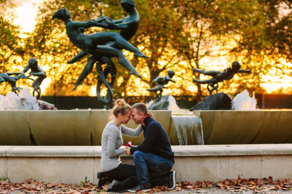 A joyful couple embracing tightly in Hyde Park, London, just moments after a surprise marriage proposal.