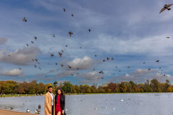 A newly engaged couple posing together on a scenic walkway in Kensington Gardens, London.
