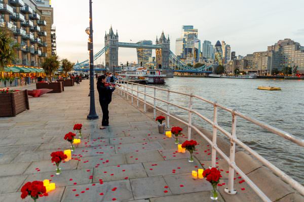 A spectacular marriage proposal setup overlooking Tower Bridge in London, featuring glowing candles, elegant floral arrangements, and a live violinist.